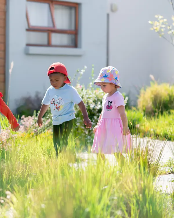 Three Preschool children holding hands and walking through tall grass