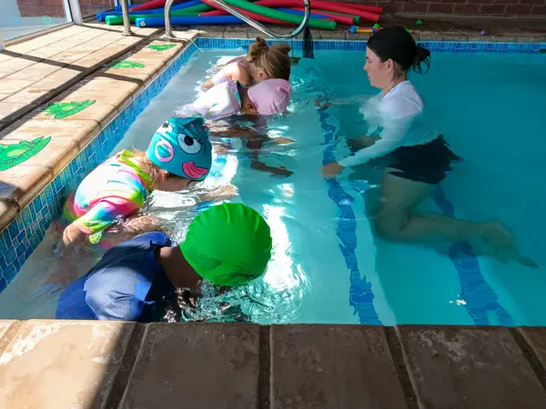 Little swimmers in bright caps having a lesson with their teacher in the heated learn-to-swim pool