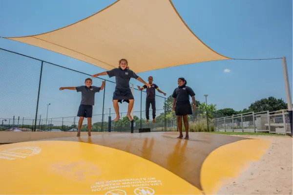 Children leaping on the yellow jumping pillow under a shade sail