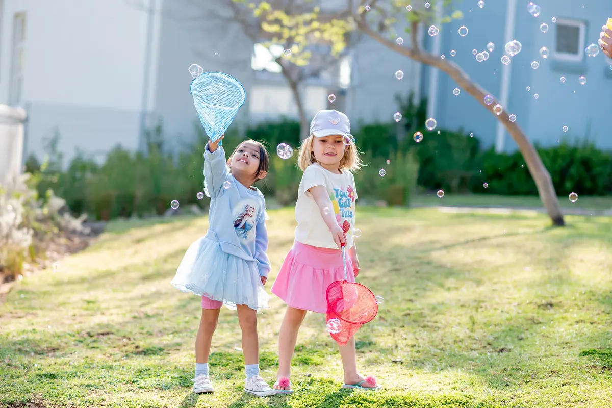 Two Preschool girls with butterfly nets catching bubbles on the lawn