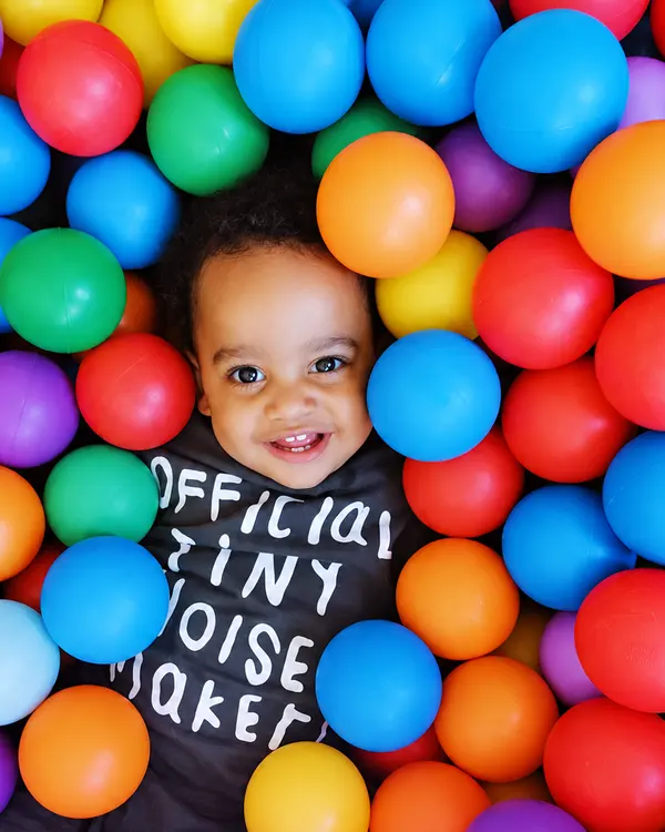 A smiling toddler peeking out of a ball pit full of brightly coloured balls