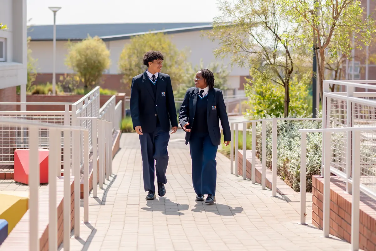 Two High School students in blazers walking and talking along a garden walkway