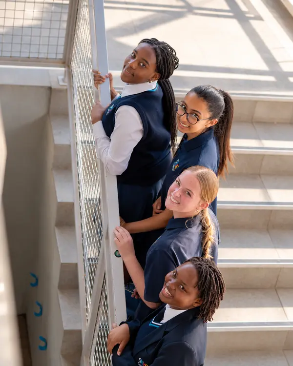 Four High School students smiling up at the camera from a sunny stairwell