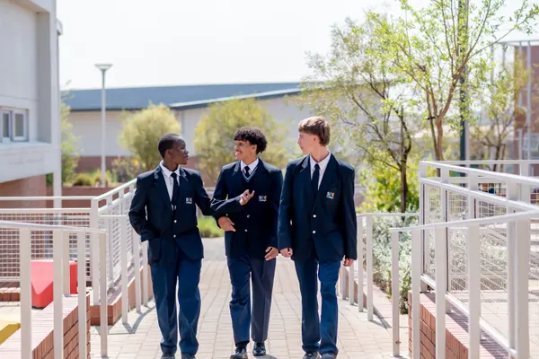 Three High School students in blazers walking together along a garden walkway