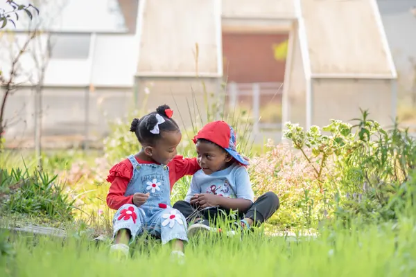 Two Preschool toddlers in sunhats sitting together in the long grass