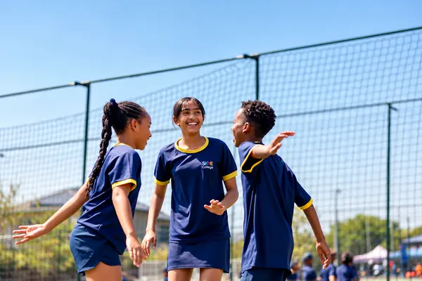 Three Senior Prep children in sports kit laughing together on the field