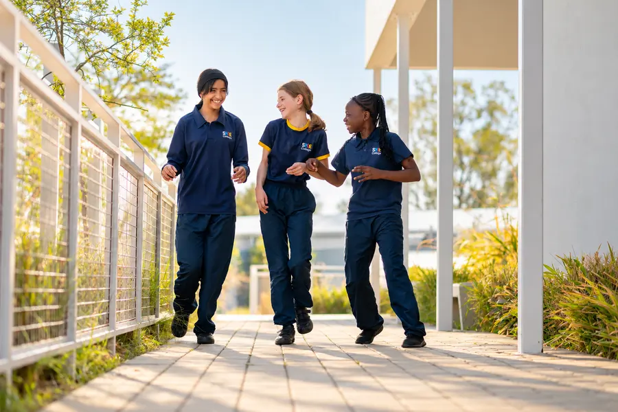 Three students walking and laughing together along a sunny garden walkway