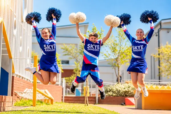 Three cheerleaders jumping high with pom-poms in the courtyard