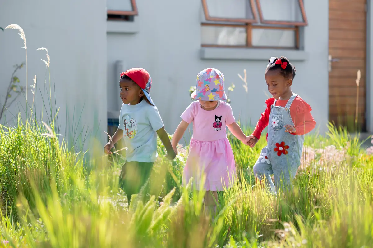 Three Preschool friends holding hands in the long grass