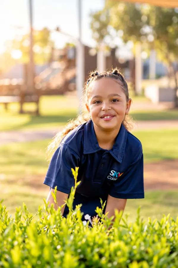 A smiling Prep girl kneeling in the garden