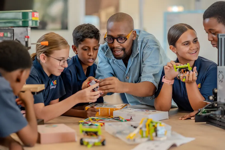 A teacher leaning in with smiling students as they build and test small robots together