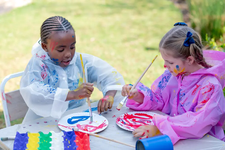 Two girls in painting smocks painting together at an outdoor table