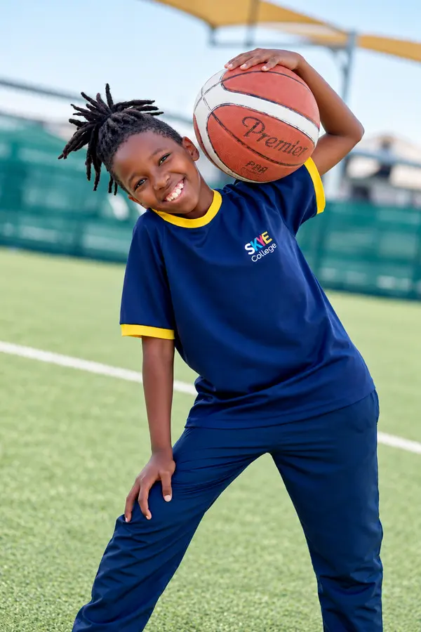 A grinning boy holding a basketball on his shoulder