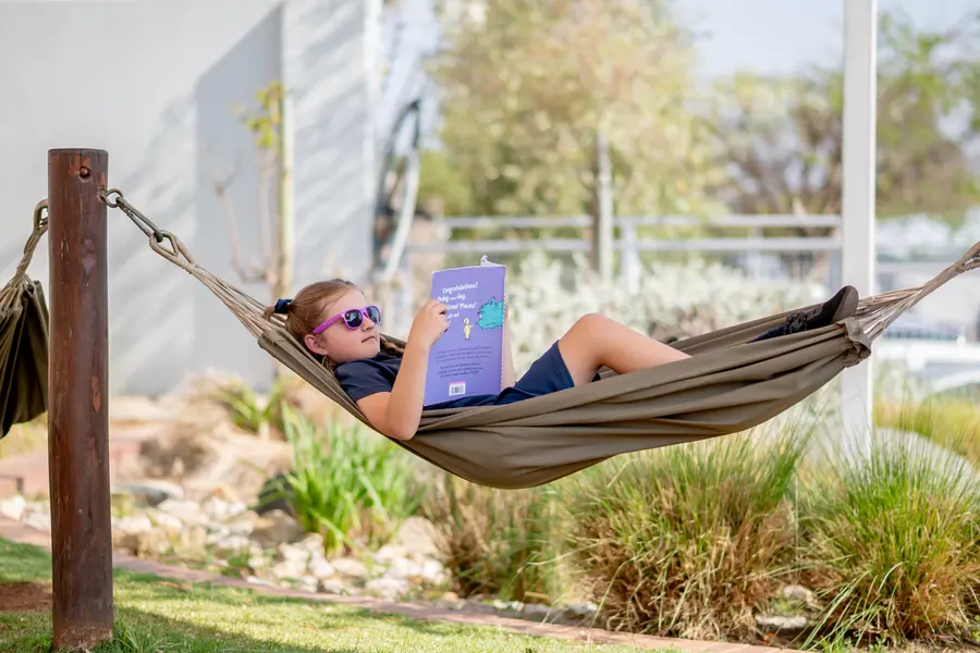 A girl in sunglasses reading in a hammock in the garden