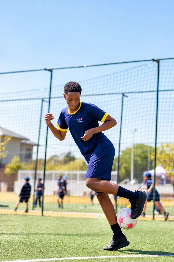 A Prep boy leaping to kick a soccer ball on the astro