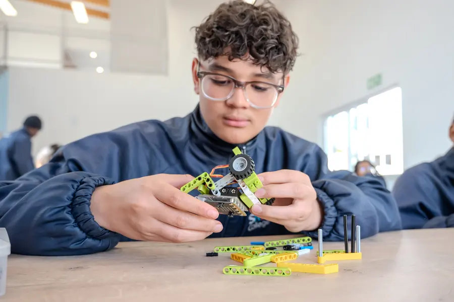 A student concentrating as he builds a small robot from construction pieces