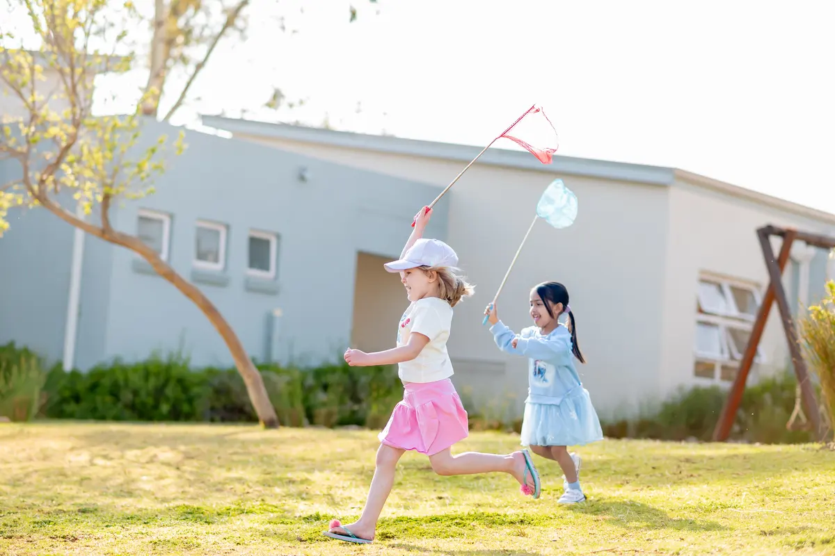 Two Preschool girls running across the lawn chasing bubbles with butterfly nets