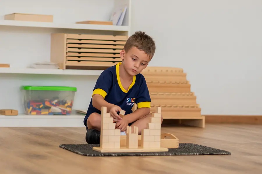 A boy concentrating as he builds with wooden Montessori blocks on a work mat