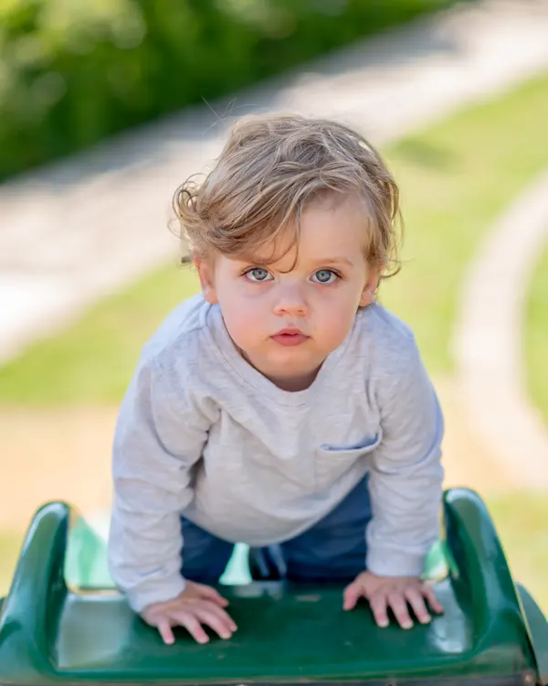 A baby crawling down a green slide, looking up at the camera